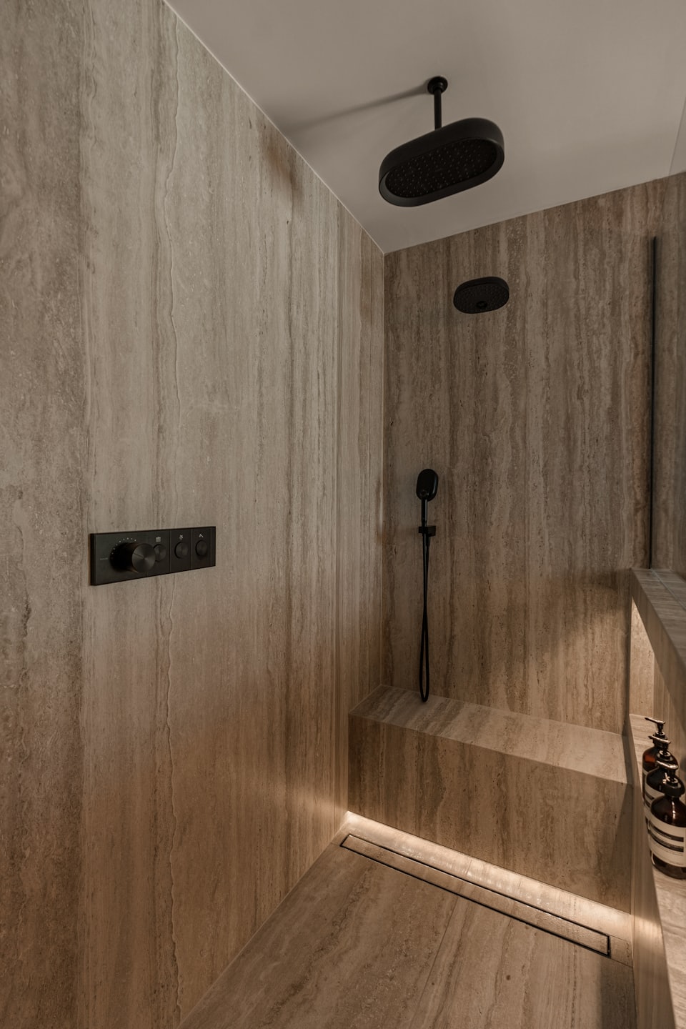 Moderna doccia walk-in con pietra travertino e rubinetteria nero opaco.