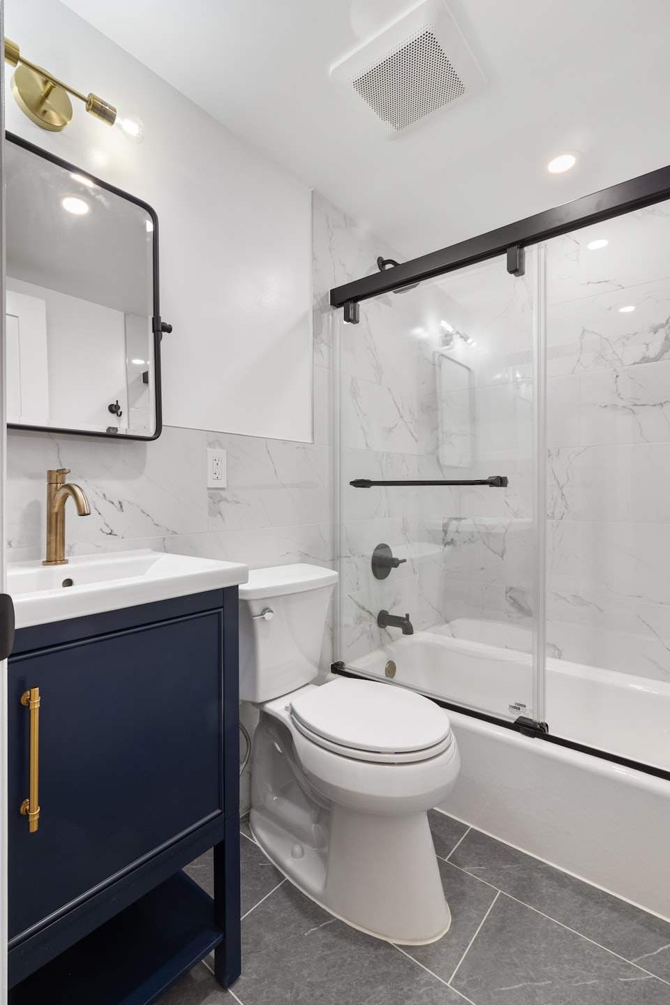 Bagno moderno con mobiletto blu navy, rubinetto dorato e piastrelle di marmo.