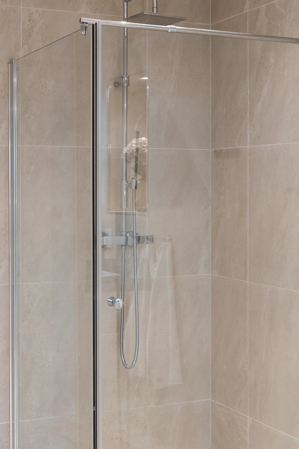 Doccia moderna con rubinetteria cromata e pareti piastrellate color beige.